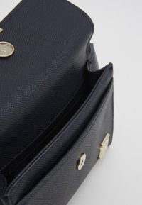 Námořnická texturovaná kožená taška se zavíráním na klopu, zlatými kovovými doplňky a jednou viditelnou vnitřní kapsou. Kompaktní design s elegantním tvarem.