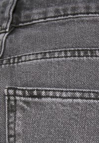 Tela de mezclilla gris con un primer plano de hilos texturizados, costuras visibles y un detalle de bolsillo. Superficie suave con un ligero brillo.