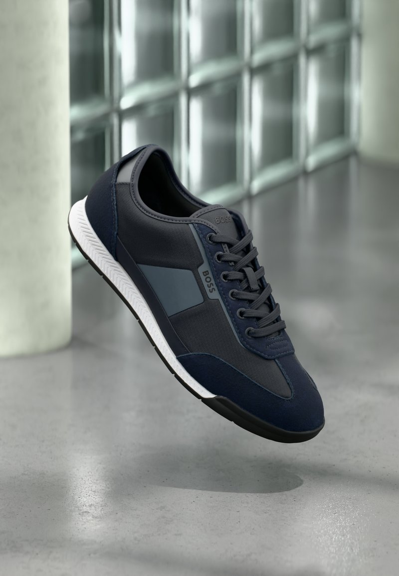 Navy zilās sporta kurpes ar tekstila un ādas kombināciju, piedāvājot gludu dizainu, baltu zolīti un smalku logotipa akcentu.