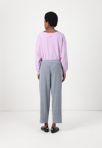 Cămașă lavandă cu mânecă lungă și decolteu rotund, cu o bandă elastică la talie, asortată cu pantaloni gri cu picioare largi și pantofi negri slip-on.