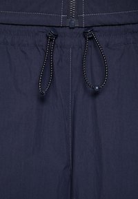 Diepblauwe stoffen shorts met een ritsluiting, elastische tailleband en koorddetail met contrasterende stiksels.