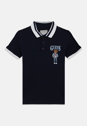 Polo azul marino con cuello y detalles en las mangas en blanco. Presenta un bordado con la imagen de un oso y el logo "GUESS" en la parte delantera.