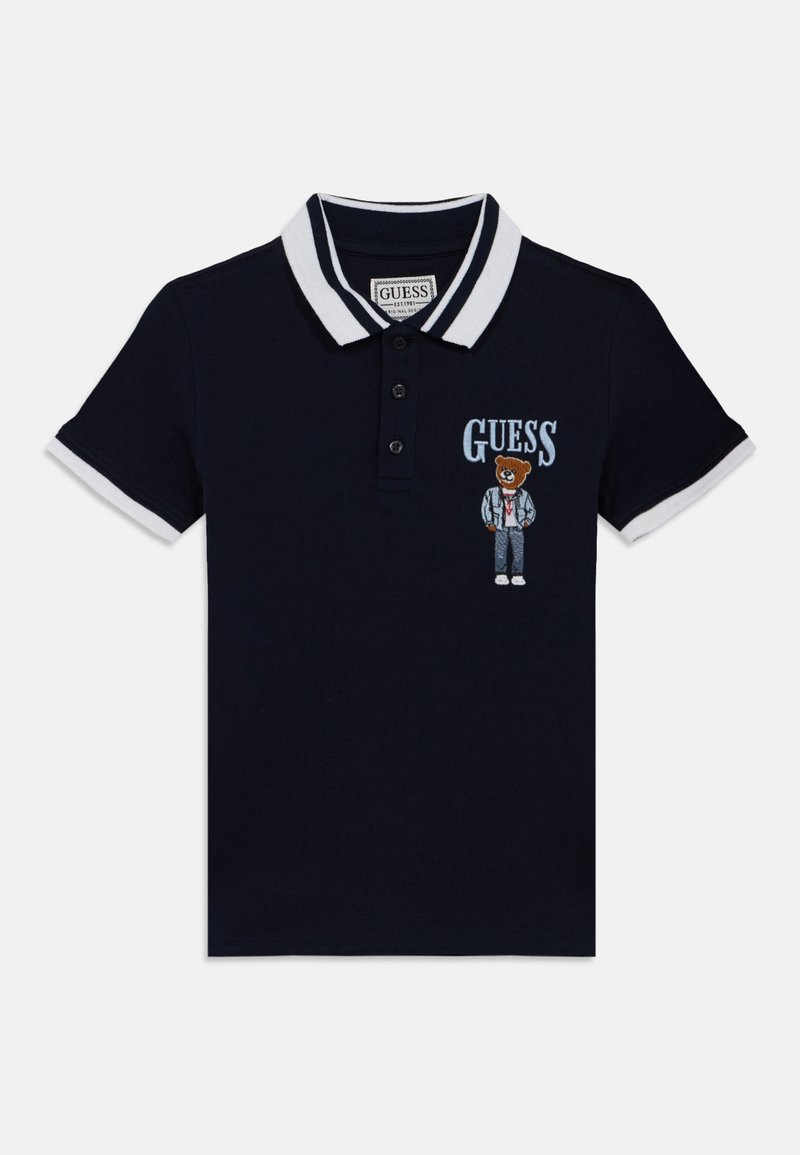 Μπλε σκούρο πόλο μπλουζάκι με λευκό γιακά και λεπτομέρειες στα μανίκια. Διαθέτει κεντητό σχέδιο αρκούδας και λογότυπο "GUESS" στο μπροστινό μέρος.