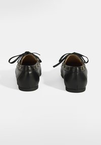 Schwarze Lederschuhe mit glatter Oberfläche, ausgestattet mit Schleifenbändern und goldenen Hardware-Akzenten an den Seiten. Abgerundete Absätze und ein klassisches Design.