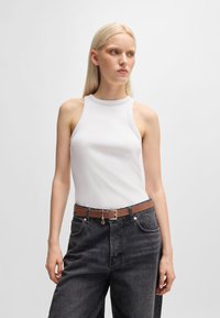 Top a righe bianco con collo alto e fori per le braccia ampi, abbinato a pantaloni grigi a vita alta e una cintura marrone con fibbia metallica.