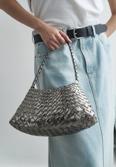 Geweven metallic zilveren handtas met een gebogen vorm en een gevlochten handvat, gecombineerd met lichtblauwe denim en een zwarte riem.