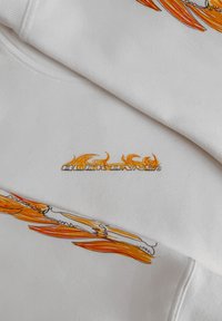 Witte sweatshirt met kleurrijke vlamgraphics en het woord "blockenns" in gestileerde tekst. Zacht, textuurstof met zichtbare stiksels.