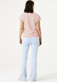 Gestreiftes, kurzärmliges Oberteil in Weiß mit roten Streifen, kombiniert mit hellblauen Schlagjeans. Das Outfit zeichnet sich durch einen lässigen Schnitt und weichen Stoff aus.