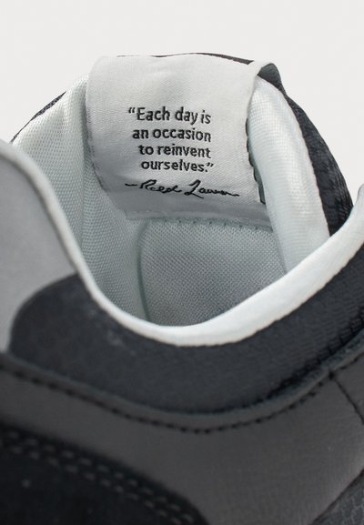 Citaat binnenin een zwart-witte sneaker zegt: "Elke dag is een gelegenheid om onszelf te herontdekken." ondertekend door Reek Lawn.