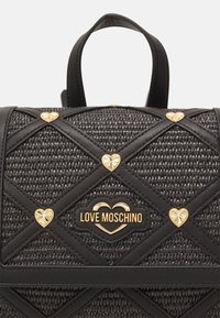 Czarna pleciona torebka z pikowanym wzorem, z złotymi akcentami w kształcie serca i plakietką z logo. Posiada dwa uchwyty i teksturowane wykończenie.