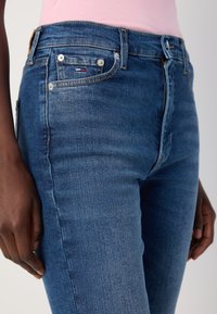 Sittende blå denim jeans med en lett falmet vask, fem lommer, og en liten merkeakutt på frontlommen.