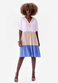 Kleurgeblokte jurk met een witte top, beige middelstuk en een blauwe rok. V-hals met textuurdetail, korte mouwen, vloeiende stof.
