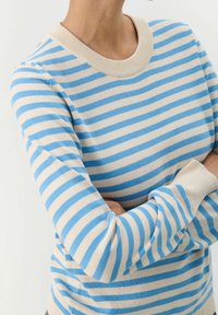 Pull rayé avec des lignes horizontales bleues et crème, col rond côtelé, texture douce et manches longues ajustées.