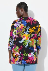 Svart blommig topp med 3/4 ärm och livfulla flerfärgade mönster. Har rund halsringning och böjd nederkant. Slät tygtextur.
