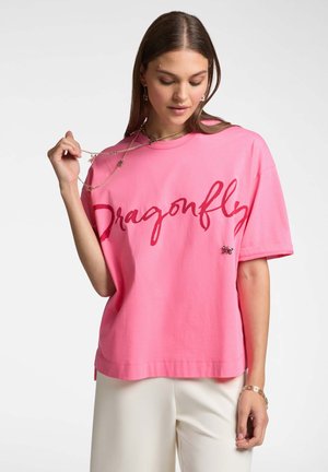 T-shirt di cotone rosa con maniche corte, caratterizzato dalla parola "Dragonfly" in rosso corsivo e un accento decorativo a forma di farfalla sulla parte anteriore.