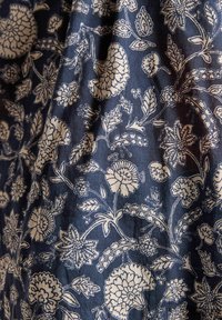 Námorná látka s zložitými bielymi kvetinovými a listovými vzormi; obsahuje rôzne tvary kvetov a podrobné akcenty v celom dizajne.