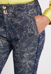 Tummansiniset kukkakuosiset farkut, joissa on valkoiset ääriviivat, kaksi nappia ja sivutasku. Suunnittelultaan tiukat ja sileä tekstuuri.