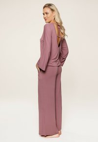 Set di loungewear a maniche lunghe in malva presenta un'apertura sul retro con un nodo. La parte superiore ha una vestibilità rilassata, mentre i pantaloni sono a gamba larga e con tasche.