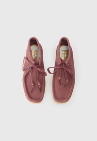 Sapatos de camurça cor-de-rosa com forma arredondada, superfície texturizada, atacadores com fecho de toggle e sola de borracha. Apresenta uma palmilha e etiqueta com marca.