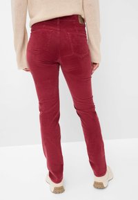 Rode corduroy broek met een slim fit, voorzien van twee achterzakken en een bruin leren label op de tailleband. Gecombineerd met beige schoenen.
