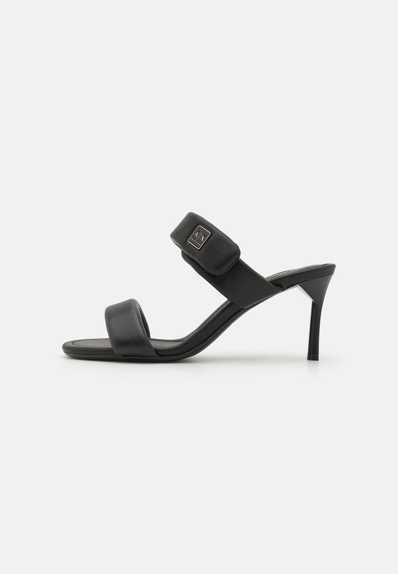 Zwarte hoge hakken sandalen met een smalle teband en een gewatteerde bovenband, met een klein decoratief logo op de band. Gladde lederen textuur.