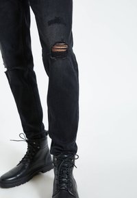 Czarne zniszczone dżinsy z dziurami na kolanach i dopasowanym kroju, w zestawieniu z czarnymi sznurowanymi botkami o teksturowanym wykończeniu i solidnej podeszwie.