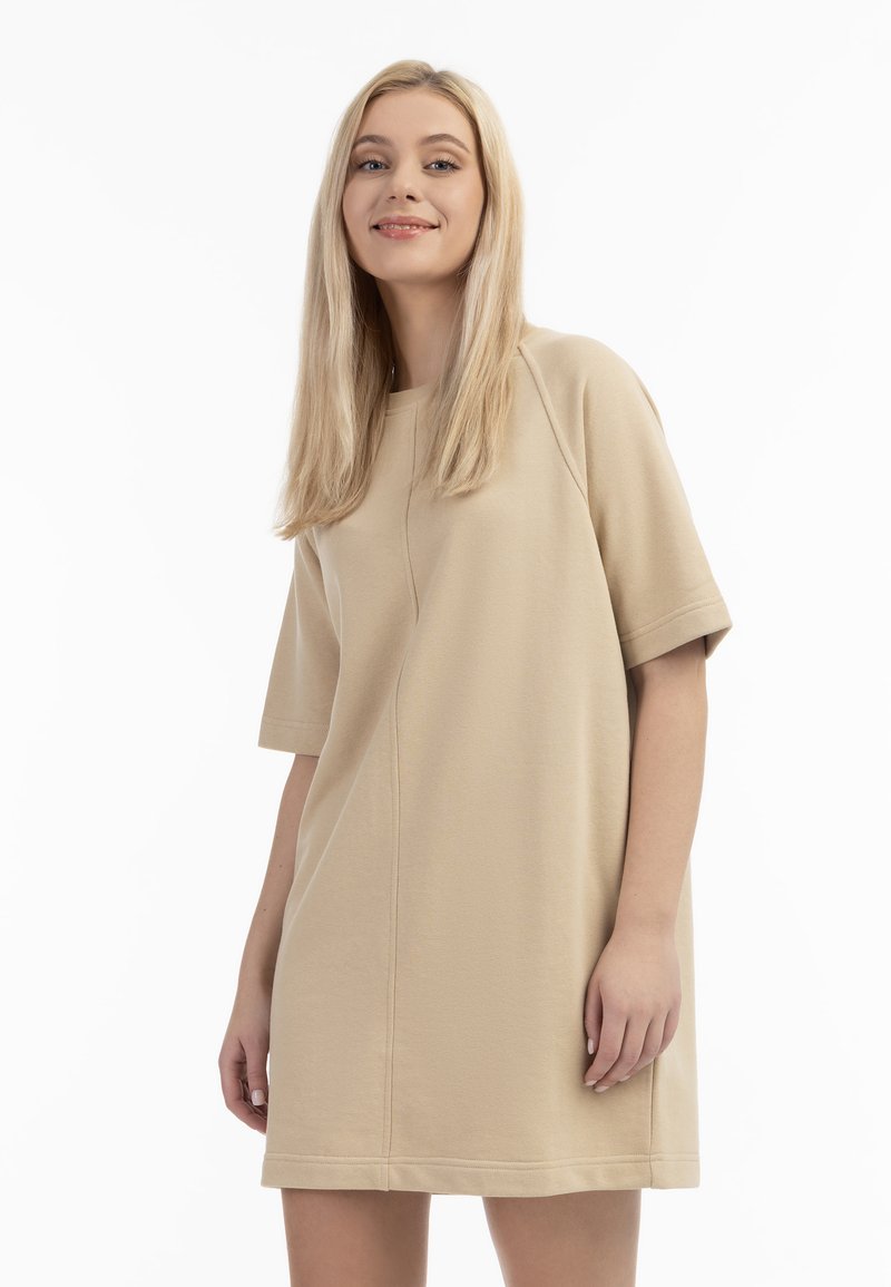 Beige bomulls-klänning med korta ärmar och avspänt snitt. Har rund halsringning och subtil sömdetaljering. Slät textur.