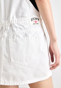 Bela denim krilo z elastičnim pasom, z zadnjim žepom in oznako DKNY, prišito na pasu. Preprost dizajn, sproščen stil.