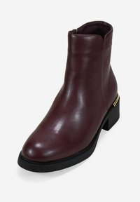 Bottine en cuir bordeaux avec un bout arrondi, fermeture éclair sur le côté, semelle en caoutchouc noir et accent doré sur le talon. Texture lisse.