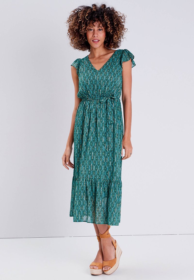 Green patterned maxi dress with a V-neck, short ruffled sleeves, a cinched waist, and a tiered skirt, paired with tan wedge sandals.