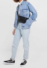 Chaqueta de mezclilla azul claro con dos bolsillos en el pecho, sudadera blanca con capucha debajo, combinada con jeans claros y bolso cruzado negro, complementado con zapatillas negras.