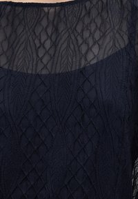 Μπλε ρουά φόρεμα με διακοσμητικές λεπτομέρειες μπροστά με κέντημα σε μοτίβο διαμαντιών και φύλλων και διαφανές πλέγμα στο πάνω μέρος του στήθους.