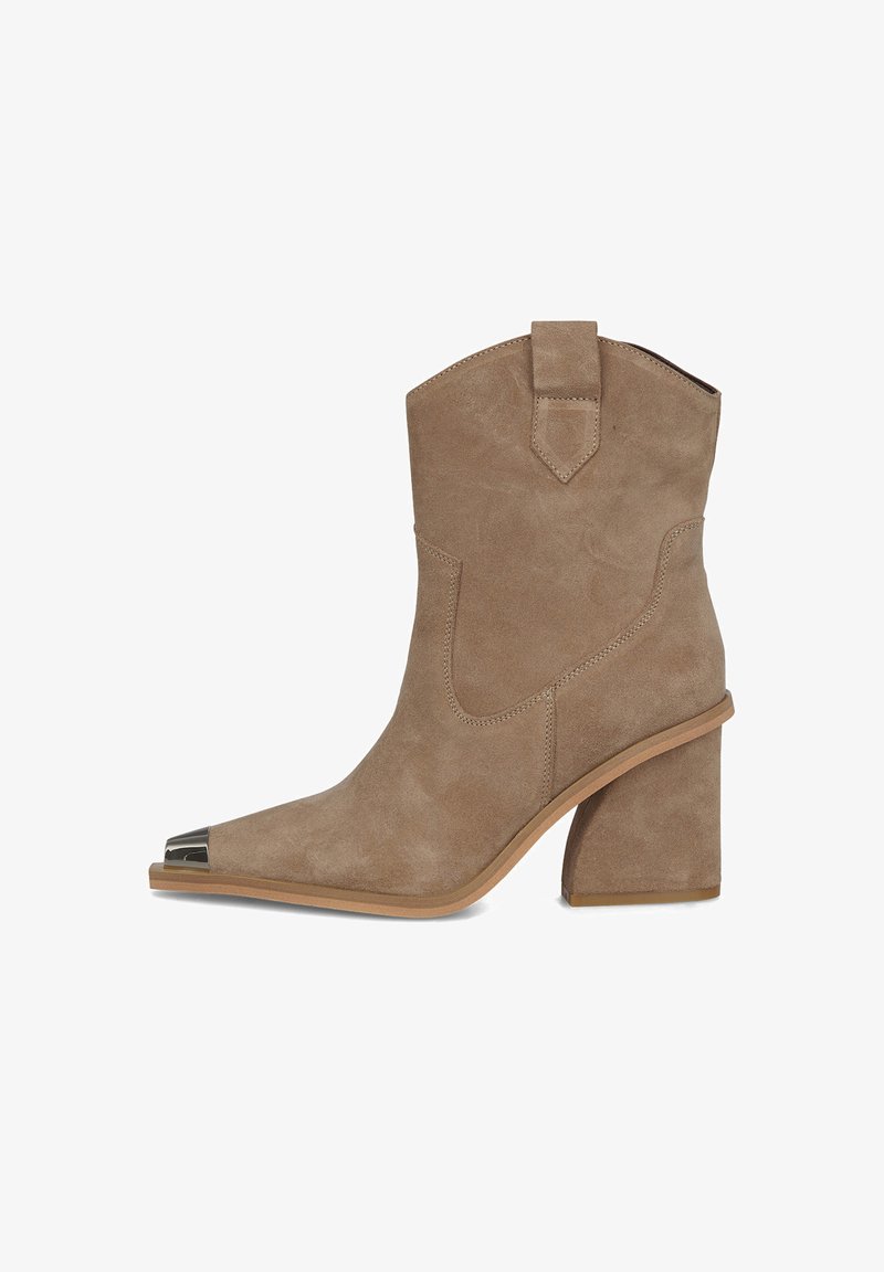 Bota de ante marrón hasta el tobillo con punta afilada, que presenta un acento metálico en la puntera y un tacón grueso. Silueta estructurada con costuras laterales.