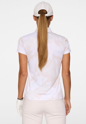 Polo a maniche corte di colore bianco con un motivo sottile. Il materiale sembra liscio con una texture leggera, abbinato a pantaloni da golf chiari e guanti.
