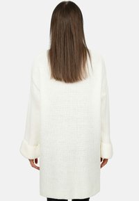 Cardigan bianco lavorato a maglia con maniche lunghe e polsini a coste, caratterizzato da una vestibilità ampia e un motivo testurizzato. La vista posteriore mostra il dettaglio della cucitura centrale.