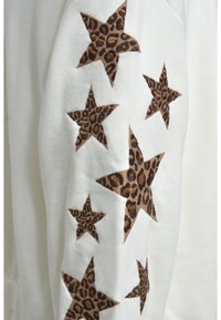 Helles Creme Sweatshirt mit sieben braunen Leopardprint-Sternen, die entlang des Ärmels gestickt sind. Weicher Stoff mit einer lässigen Passform.
