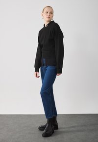Black knitted sweater with a high neckline, paired with dark blue straight-leg jeans. The outfit is completed with chunky black ankle boots.