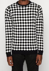 Černobílý svetr s diamantovým vzorem, kulatým výstřihem, žebrovaným lemem a manžetami, vyrobený z měkké pletené látky.