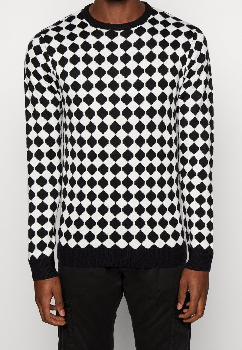 Černobílý svetr s diamantovým vzorem, kulatým výstřihem, žebrovaným lemem a manžetami, vyrobený z měkké pletené látky.