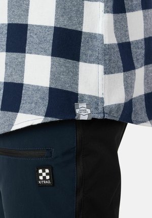 Navy and white checked shirt fabric with a denim patch tag. Black pants with a zippered pocket and an X-TRAIL logo patch in white.