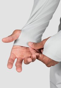 Hellgraues Langarmshirt mit eng anliegenden Manschetten, glatter Textur und einer engen Passform um die Handgelenke. Hände, die die Ärmel anpassen.