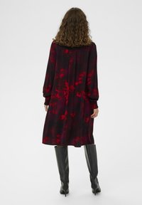 Długa czarna sukienka z czerwonym kwiecistym wzorem, z długimi rękawami i marszczonymi mankietami, zestawiona z czarnymi botkami do kolan. Miękka tekstura materiału.