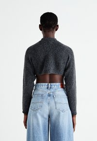 Pulover scurt gri cu mâneci lungi, textură de lână, asortat cu blugi deschiși la culoare, cu talie înaltă, având buzunare la spate și o etichetă din piele.