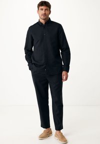 Zwarte langetermijn shirt met een button-down kraag, gecombineerd met zwarte op maat gemaakte broek en beige instapschoenen. Soepele stoftextuur.