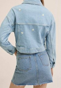 Ljust blå denimjacka med blommig brodyr på baksidan, ihop med en matchande denimkjol med fransad fåll och fickor.