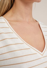 Randig tröja i stickad stil med djup V-ringning, vit med ljusbeiga horisontella ränder, slät struktur och kort ärm design.