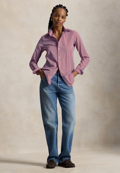 Chemise à rayures rouges et blanches à boutons, associée à un jean bleu clair à jambes droites, avec une coupe décontractée et des revers roulés.