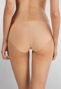 Nude naadloze ondergoed met een lage taille, een gladde textuur en geen zichtbare naden, vanaf de achterkant weergegeven tegen een neutrale achtergrond.