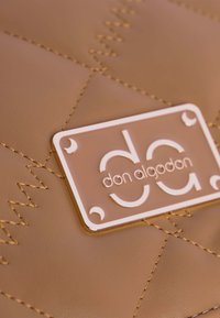 Bolso de cuero acolchado marrón con herrajes en tono dorado, que presenta una placa de logo rectangular y patrones de costura contrastantes.