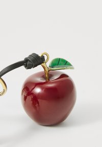 Red glass apple-shaped accessory with a gold stem and green leaf. Attached black leather strap. Glossy finish with a smooth texture.